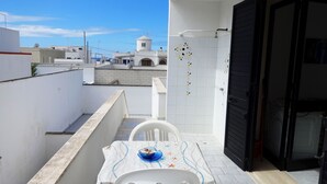 A balcony with a table set for two, a white chair, and a blue bowl.