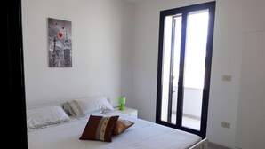 A bedroom with a bed, pillows, a nightstand, a lamp, and a window with blinds.
