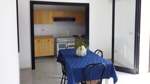 A compact kitchen with wooden cabinets and a white stove, a dining table with a blue tablecloth, and a potted plant.