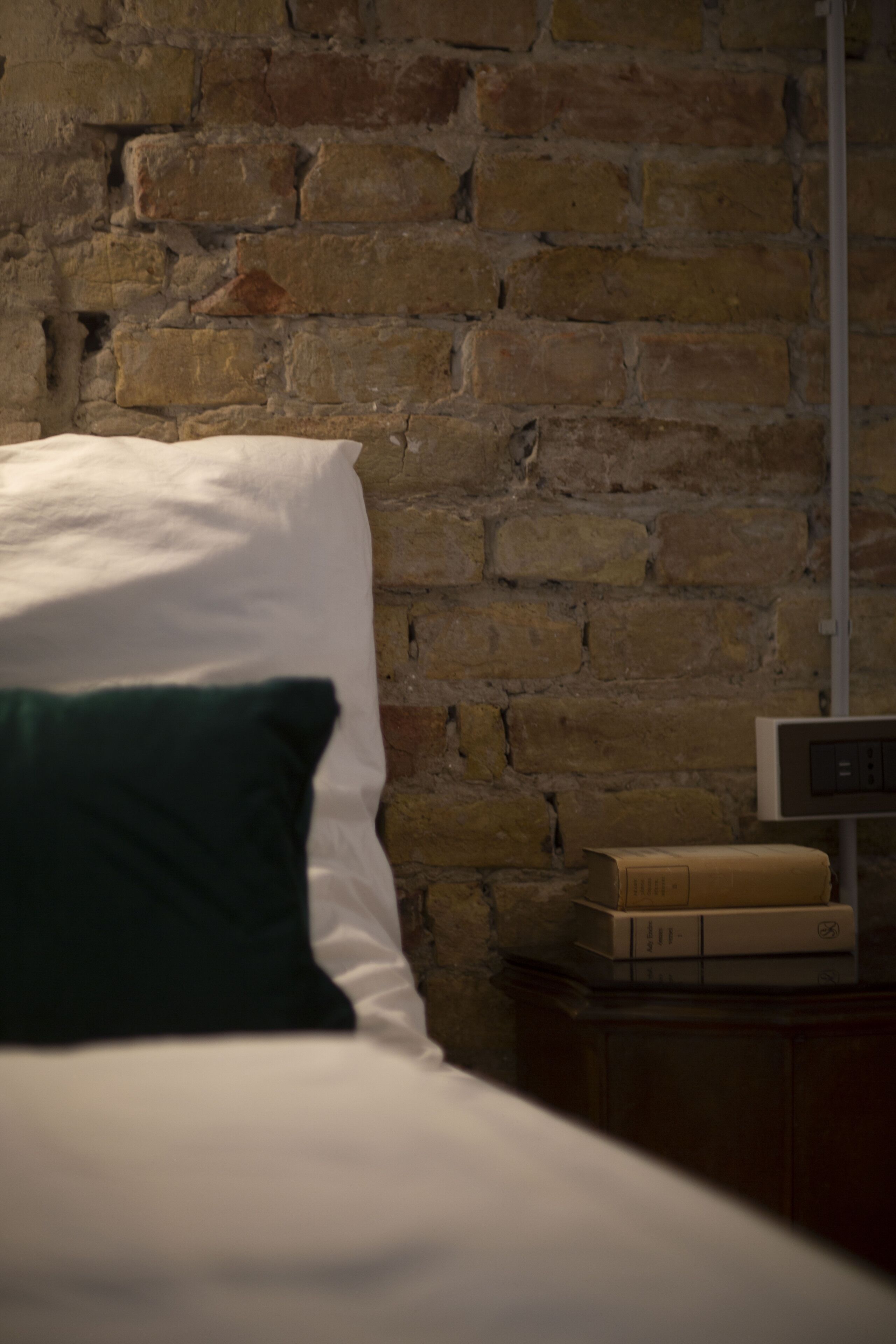 A bed with white bedding and a green pillow against a brick wall.