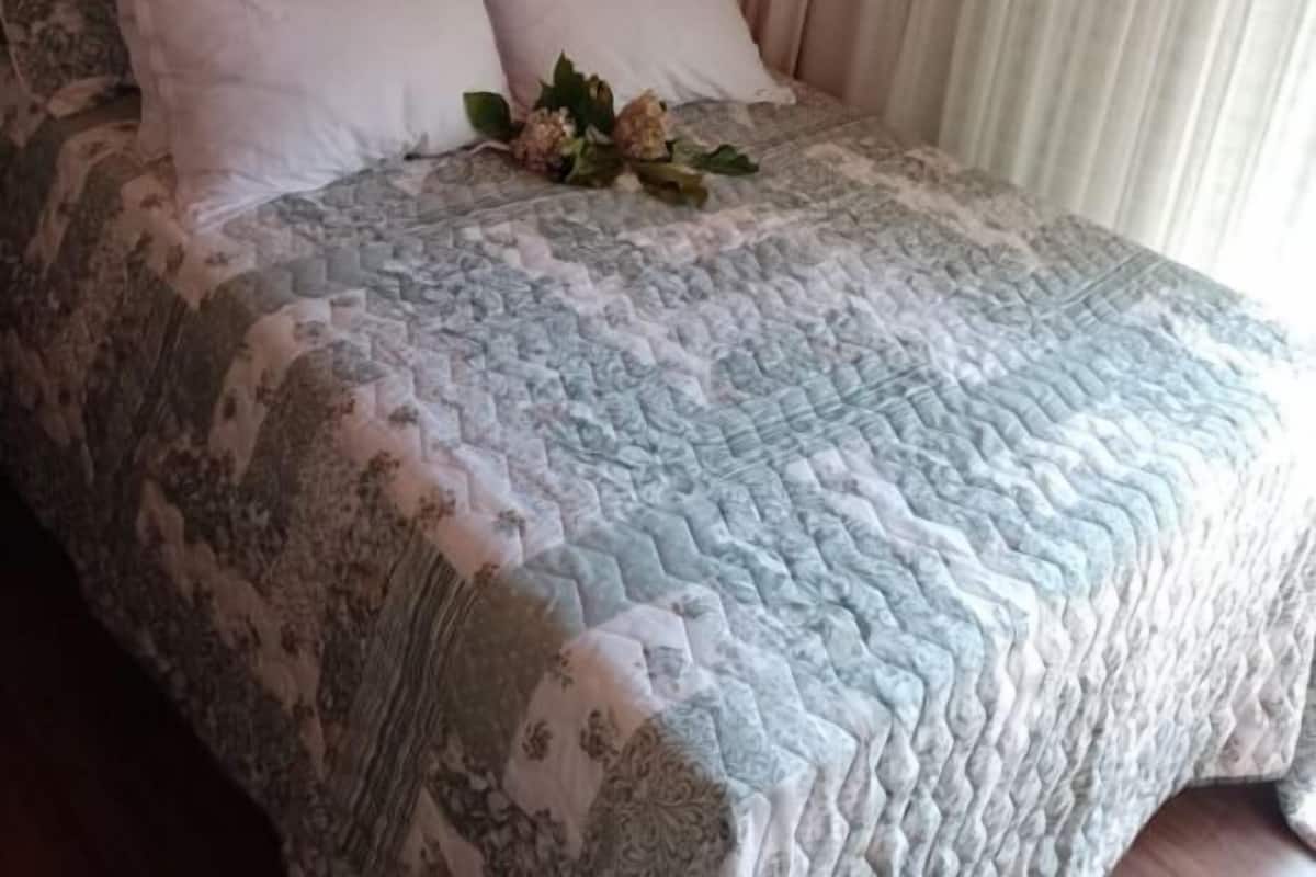 A bedroom with a bed, a headboard, a window with curtains, and a floral arrangement on the bed.