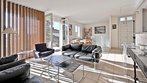 Una sala de estar moderna con un sofá de cuero, una mesa de centro de vidrio y un comedor con una mesa y sillas blancas.