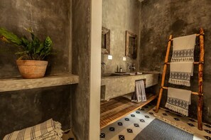 A bathroom with a concrete wall, a wooden shelf with a potted plant, a wooden ladder with towels, and a tiled floor.
