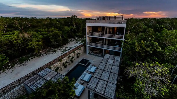 Un bâtiment moderne à plusieurs étages, doté d’une piscine et d’un espace extérieur aménagé, le tout entouré d’une végétation luxuriante.