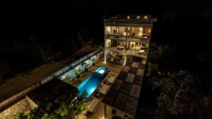 Un immeuble à plusieurs étages doté d’une piscine au niveau du rez-de-chaussée, entouré d’une terrasse en bois et d’un mur en pierre.