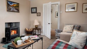 A cozy living room with a fireplace, a sofa, a coffee table with a tray of mugs, and a door leading to another room. - Wild Rose in rural location with lovely views on a working farm with walks (Jedburgh)