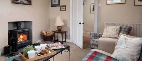 A cozy living room with a fireplace, a sofa, a coffee table with a tray of mugs, and a door leading to another room.