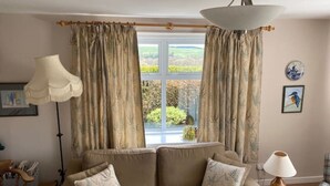 A living room with a beige sofa, two matching cushions, a floor lamp, and a table lamp. - Wild Rose in rural location with lovely views on a working farm with walks (Jedburgh)