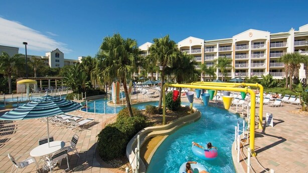 A resort pool area with a water slide, lounge chairs, and umbrellas.