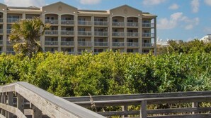 A multi-story hotel with balconies, surrounded by lush greenery and a wooden walkway leading to the entrance.