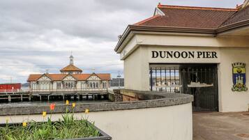 Um edifício com a placa "DUNOON PIER", estilo arquitetônico tradicional, um cais que se estende para a água e uma pequena área de jardim com tulipas.