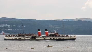 A large, stationary ferry with multiple decks, passengers, and a mountainous backdrop.
