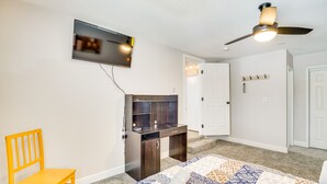 Ein Schlafzimmer mit Bett, Schreibtisch, Stuhl, Fernseher und Deckenventilator.