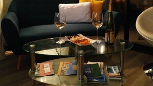 A cozy living area with a dark blue sofa, a glass coffee table, two wine glasses, a bottle of wine, and a plate of fruit.