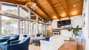 A spacious living room with a high ceiling, large windows, and a fireplace. - Swim Spa cottage on a Private Beach (Fort Erie)