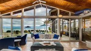 A spacious living area with a high ceiling and large windows overlooking a beach. - Swim Spa cottage on a Private Beach (Fort Erie)
