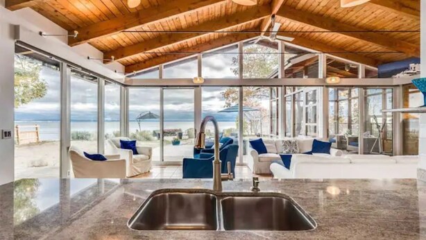A modern kitchen with a large window overlooking a beach, wooden ceiling, and a view of the sea. - Swim Spa cottage on a Private Beach (Fort Erie)