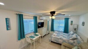 A bedroom with a bed, a desk, a chair, a ceiling fan, and a TV.