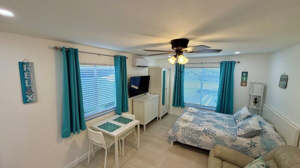 A bedroom with a bed, a desk, a chair, a ceiling fan, and a TV.