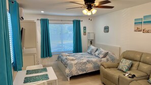 A bedroom with a bed, a sofa, a table, and a ceiling fan. - Seashell 8- Luxury Studio close to the beach! (Boynton Beach)