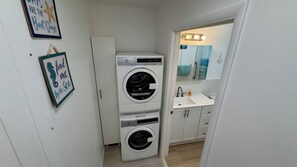 A compact laundry room with two stacked washing machines, a sink, and a mirror with lights. - Seashell 8- Luxury Studio close to the beach! (Boynton Beach)
