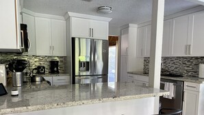 A modern kitchen with white cabinets, stainless steel appliances, and a granite countertop. - Cozy Suburban Home with huge backyard and pool! Welcome! (Miami)