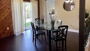 A dining area with a glass table, black chairs, a chandelier, a potted plant, and a view of the kitchen through a sliding door. - Cozy Suburban Home with huge backyard and pool! Welcome! (Miami)