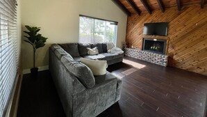 A living room with a gray sectional sofa, a potted plant, a fireplace, and a TV mounted on the wall. - Cozy Suburban Home with huge backyard and pool! Welcome! (Miami)