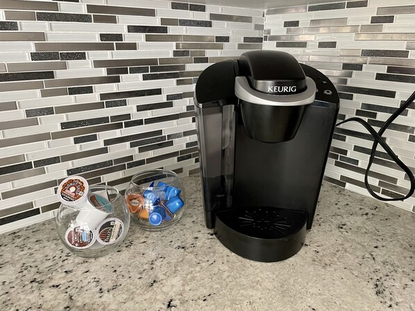A Keurig coffee maker on a kitchen counter with a coffee pod and a glass carafe.