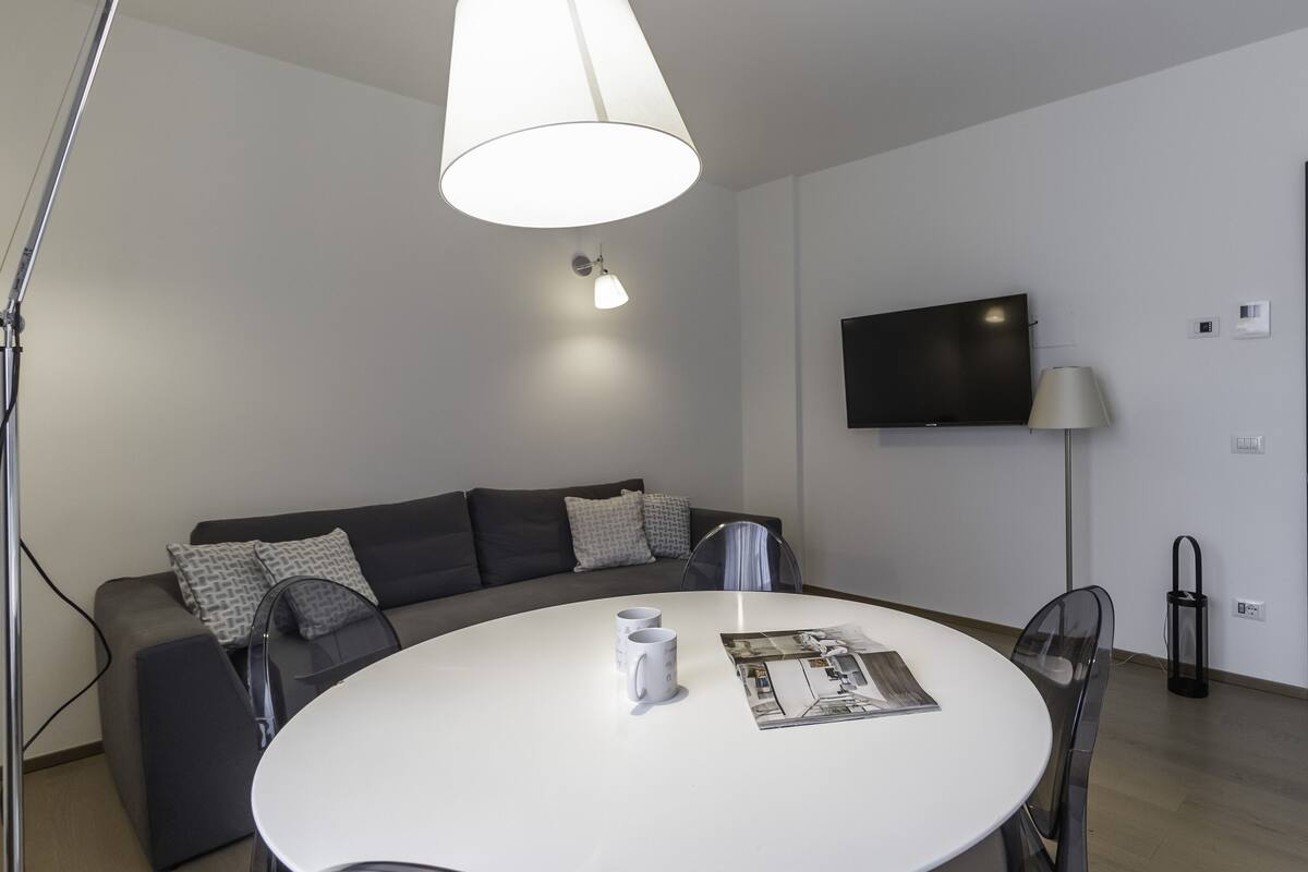 A modern living room with a sofa, a round table, a flat-screen TV, and a lamp.