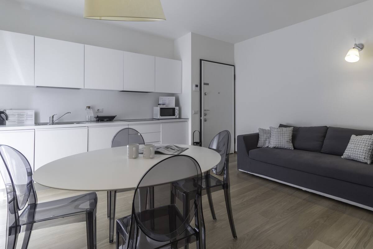 A modern living space with a dining area, a sofa, and a kitchen.