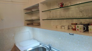 Une cuisine avec des meubles blancs, un évier et des étagères où sont rangés la vaisselle et les verres.