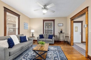 A living room with a grey sofa, a coffee table, and a ceiling fan. - West Side Historic Home (Grand Rapids)