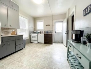 A compact kitchen with white cabinets, a stove, and a coffee maker. - West Side Historic Home (Grand Rapids)