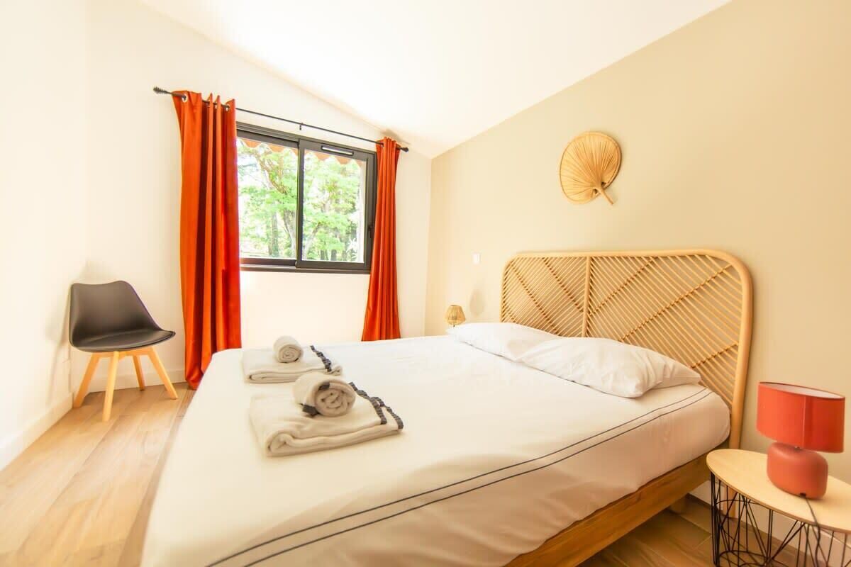 Ein Hotelzimmer mit einem Bett, einem Sessel, einem kleinen Tisch mit Lampe und einem fenster mit Vorhängen.