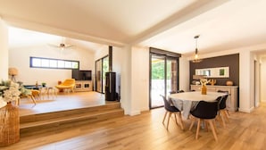 A spacious living area with a wooden floor, a dining table with chairs, a sofa, and a kitchen area with a refrigerator and a stove. - Villa Javal à Ares avec piscine chauffée (du 01/05 au 15/10) (Arès)