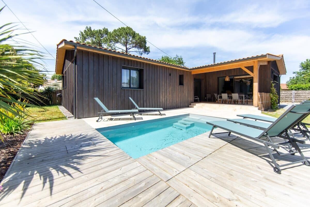 Una casa moderna con fachada de madera, piscina y mobiliario exterior.