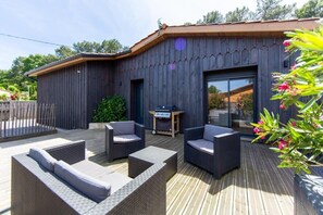 A wooden building with a deck, outdoor furniture, and a barbecue area.