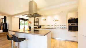 A modern kitchen with a central island, bar stools, a stainless steel range hood, and a tiled backsplash. - Villa Javal à Ares avec piscine chauffée (du 01/05 au 15/10) (Arès)