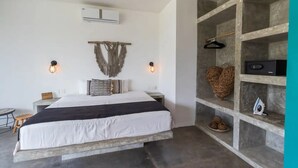 A bedroom with a large bed, a wall-mounted air conditioner, a macramé wall hanging, and a built-in shelving unit with a speaker and decorative items. - Casa Macarena 2-BR (Tulum)