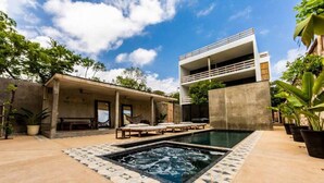 A modern outdoor pool area with a hot tub, lounge chairs, and a covered seating area. - Casa Macarena 2-BR (Tulum)