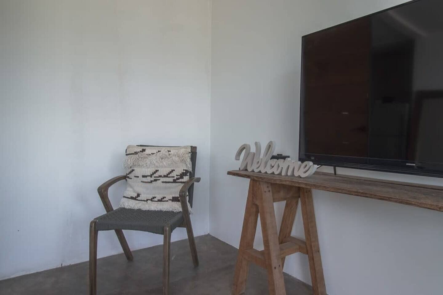 A chair with a woven backrest and a wooden table with a 'Welcome' sign.