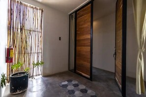 A hallway with a bamboo screen, a wooden sliding door, a potted plant, and a hexagonal tile floor.