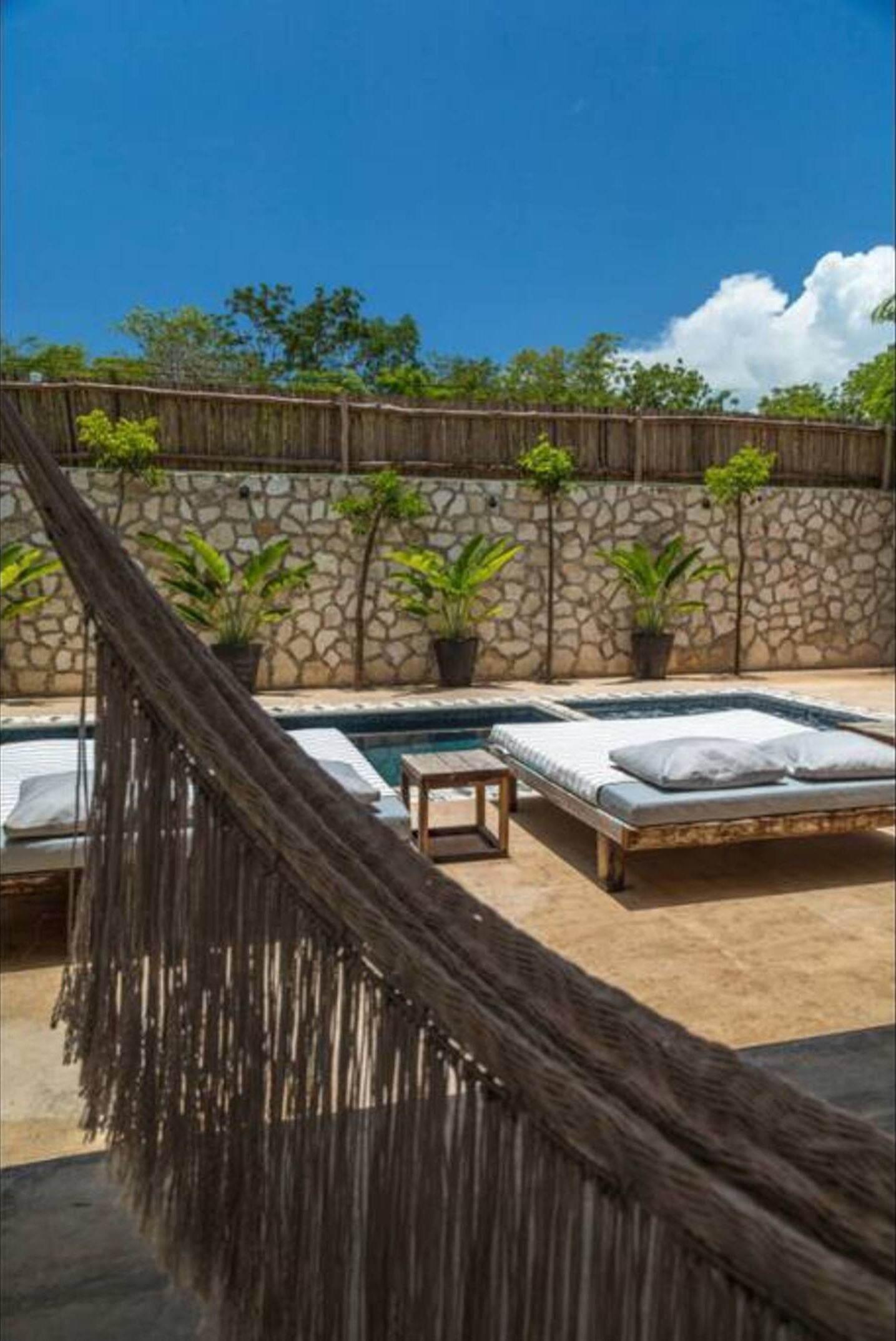 A pool area with a hammock, lounge chairs, and a stone wall.