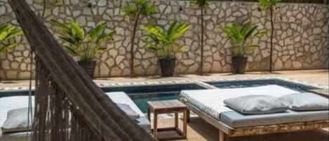 A pool area with a hammock, lounge chairs, and a stone wall.