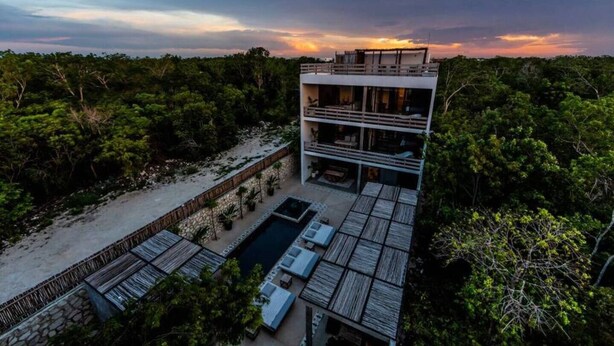 A modern multi-story building with a pool and outdoor seating area surrounded by dense greenery. - Casa Macarena 2-BR (Tulum)