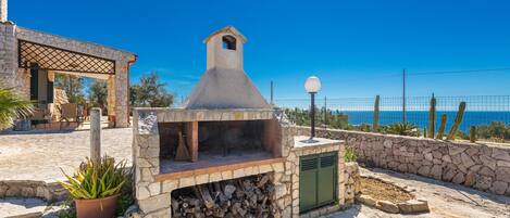 An outdoor stone barbecue area with a chimney, a potted plant, and a view of the sea.