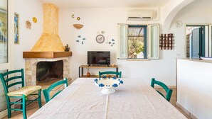 A dining area with a stone fireplace, a TV, and a table with chairs. - Stone Hill House by BarbarHouse (Torre Vado)