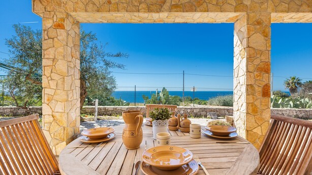 A wooden table set for dining with stone pillars and a view of the sea. - Stone Hill House by BarbarHouse (Torre Vado)