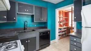 A compact kitchen with teal walls, a gas stove, a dishwasher, and a refrigerator. - Colorful Downtown Historic 2BR Shingle Home (Spartanburg)